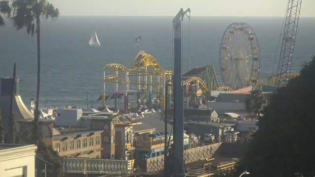 Public camera view of Santa Monica Pier, its Ferris wheel and a sailboat on the Pacific Ocean